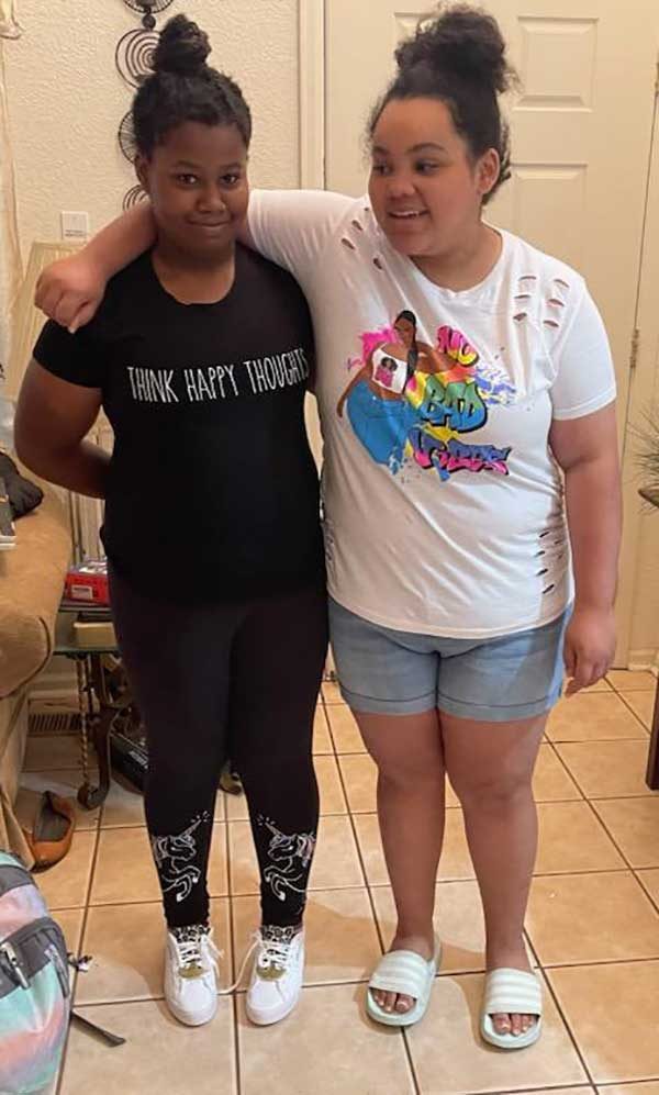 Two young family members standing arm in arm in a kitchen, one in a black t-shirt reading Think Happy Thoughts.